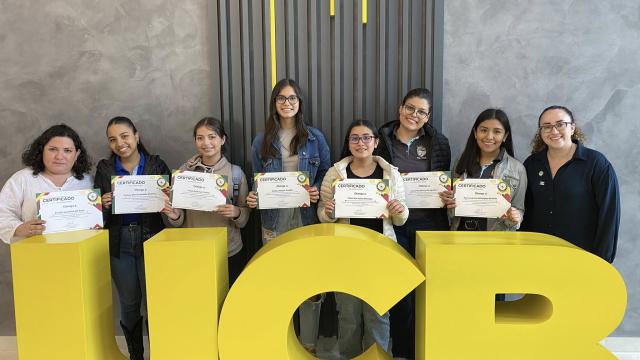 Schoolgirls holding certificates in front of a logo
