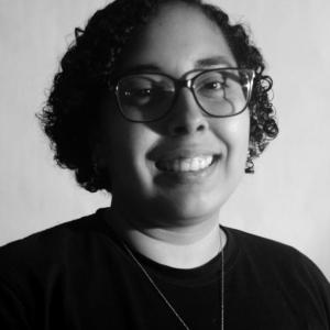 Image of myself, Pamela Figueroa, a woman with dark short curly hair and afro Latino features. I am wearing a back shirt and smiling to the camera.