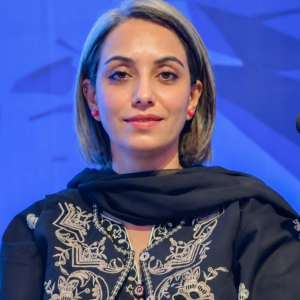 A woman sits facing the camera at a formal event.