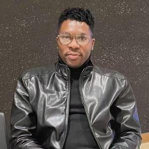 Portrait photo of Dr. Olanrewaju Ayodeji Durojaye wearing glasses and a black leather jacket, seated against a dark background
