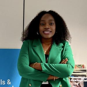 Dorothy Ngajilo standing with arms crossed, wearing a green blazer and smiling, in an office setting with a blue chemicals banner and magazines in the background.