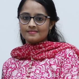 Young woman wearing glasses and a pink floral traditional outfit, smiling at the camera.