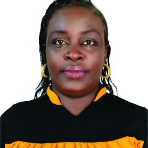 A professional head-and-shoulders portrait featuring an individual with neatly braided hair, wearing a black top with golden-yellow accents and gold hoop earrings, photographed against a plain white background with a calm and confident expression.