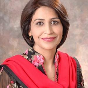 Portrait of a smiling lady with short dark brown hair, wearing a black floral outfit with a bright red scarf, against a softly textured neutral background.