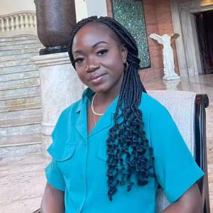 Professional portrait of a woman seated indoors, wearing a teal blouse, with braided hair and a calm, confident expression.