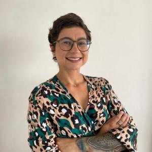Luisa has short brown hair and is wearing green glasses and a green and brown dress. 