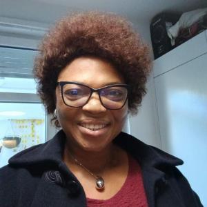 Professional headshot of Professor Evelyn Iyose Umemezia smiling in a navy blue blazer on a red top in a light background