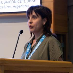 Researcher delivering an oral presentation at a scientific conference, standing behind a podium with a projected slide in the background